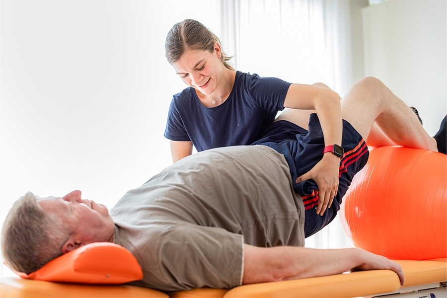 Eine Physiotherapeutin unterstützt einen Patienten bei einer Übung mit einem Gymnastikball.