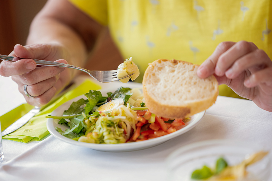 Eine Frau hält eine Scheibe Brot. Vor ihr steht ein Teller mit verschiedenen Salaten.