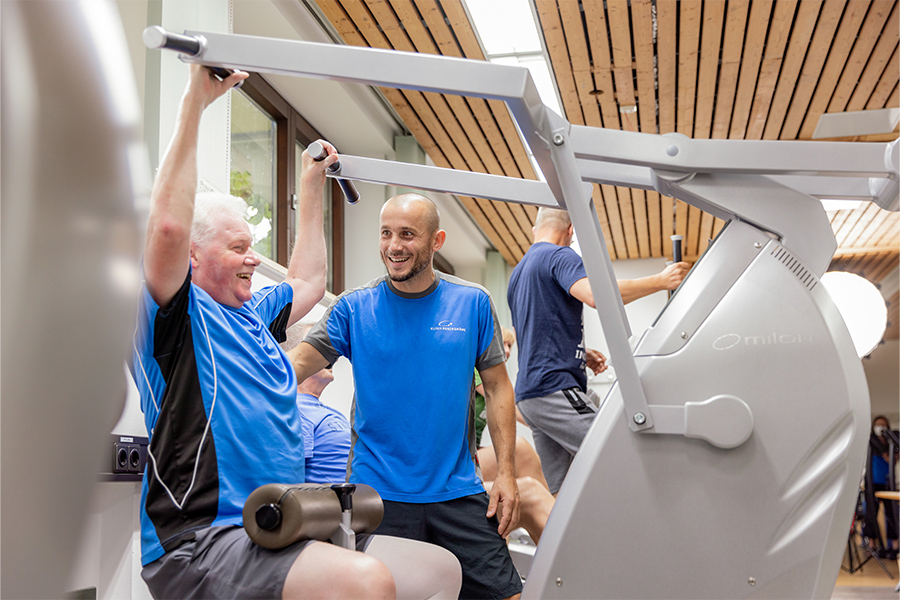 Ein Therapeut unterstützt einen Patienten an einem Trainingsgerät.